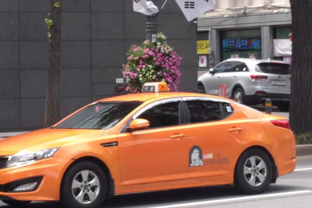 An orange taxi driving past a street with trees and Korean flags