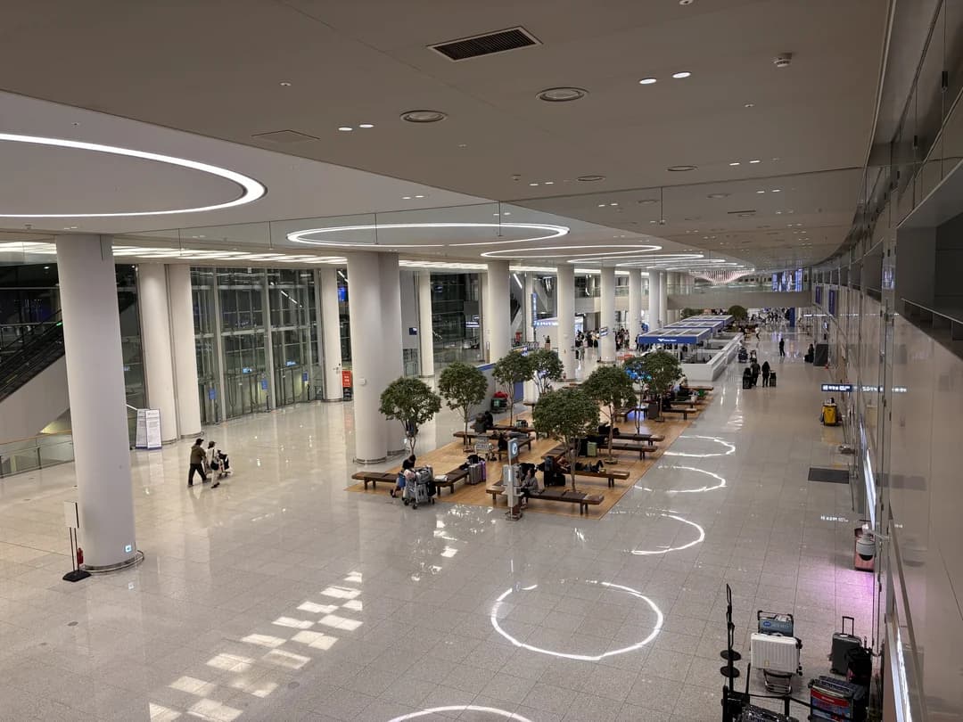 A wide airport hall with tall pillars, seating and check-in counters in the distance
