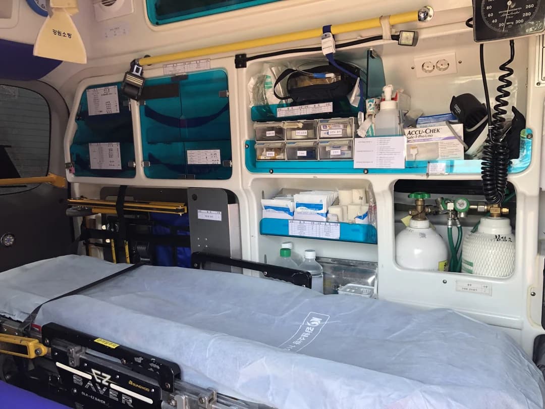 The inside of an ambulance with a stretcher, oxygen cylinders and medical equipment on the wall
